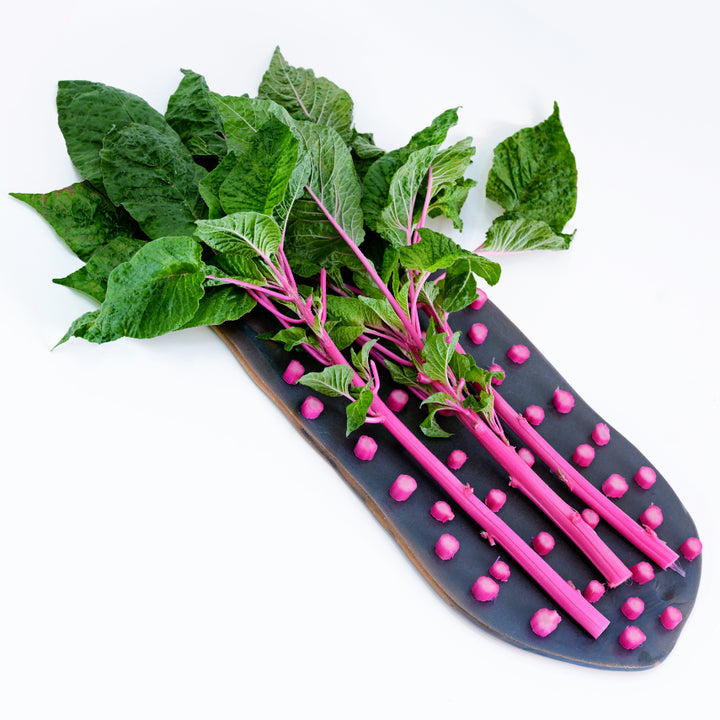 Pink Beauty Amaranth stems on black hand-made ceramic serving plate with slices surrounding the stems.