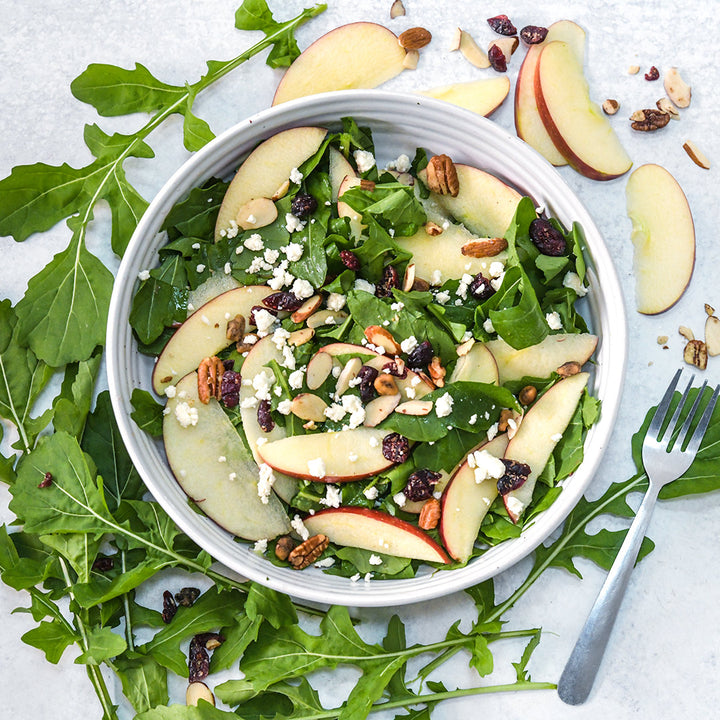 Common Arugula and apple salad in a bowl with a fork and surrounded by leaves.