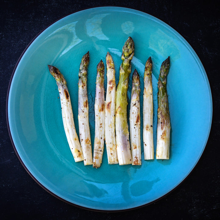 Overhead view of grilled Conovers Colossal Asparagus lined up on a blue plate on black.
