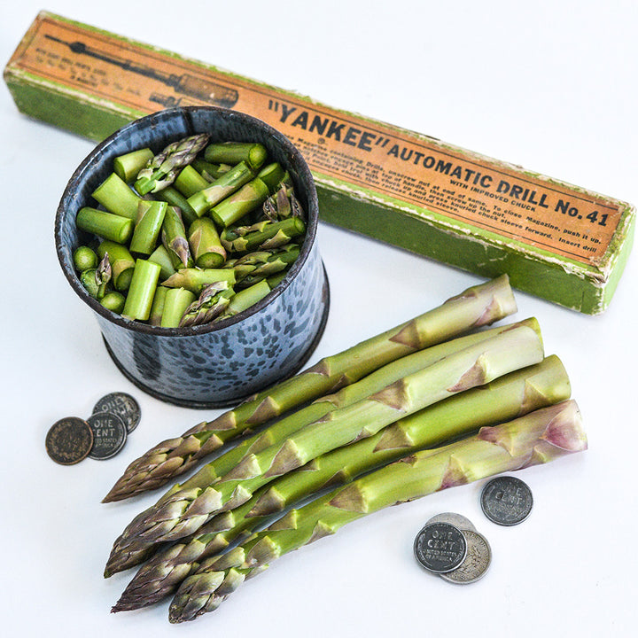 Cut and whole Conovers Colossal Asparagus with coins and props to show size on white.