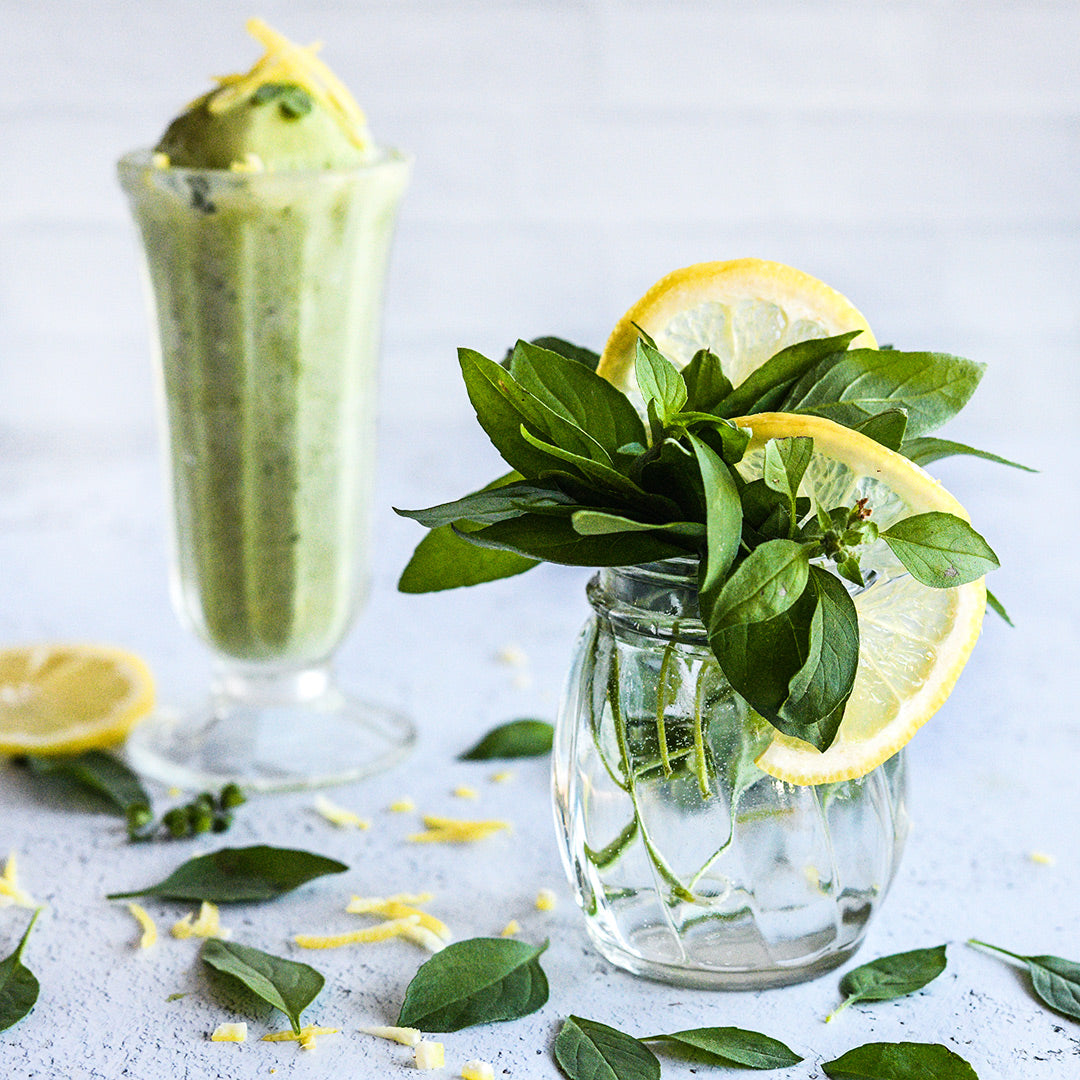 A glass vase full of Lemon Basil and lemon slices with basil ice cream in the background.