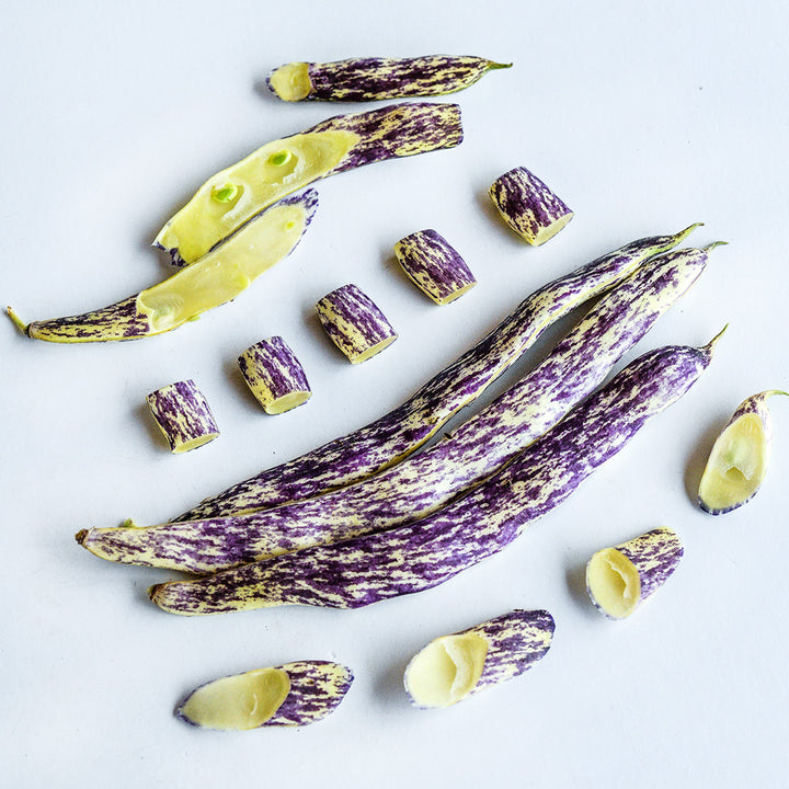 Three Dragon Tongue Beans surrounded cut beans on white background.