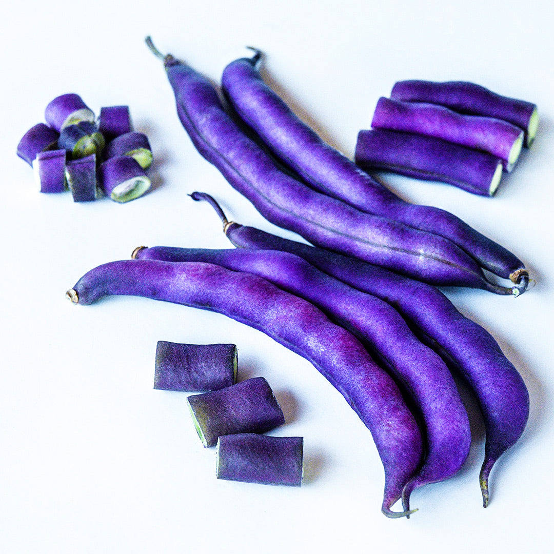 Cut and whole Purple Dove Bush Beans arranged on a white background.