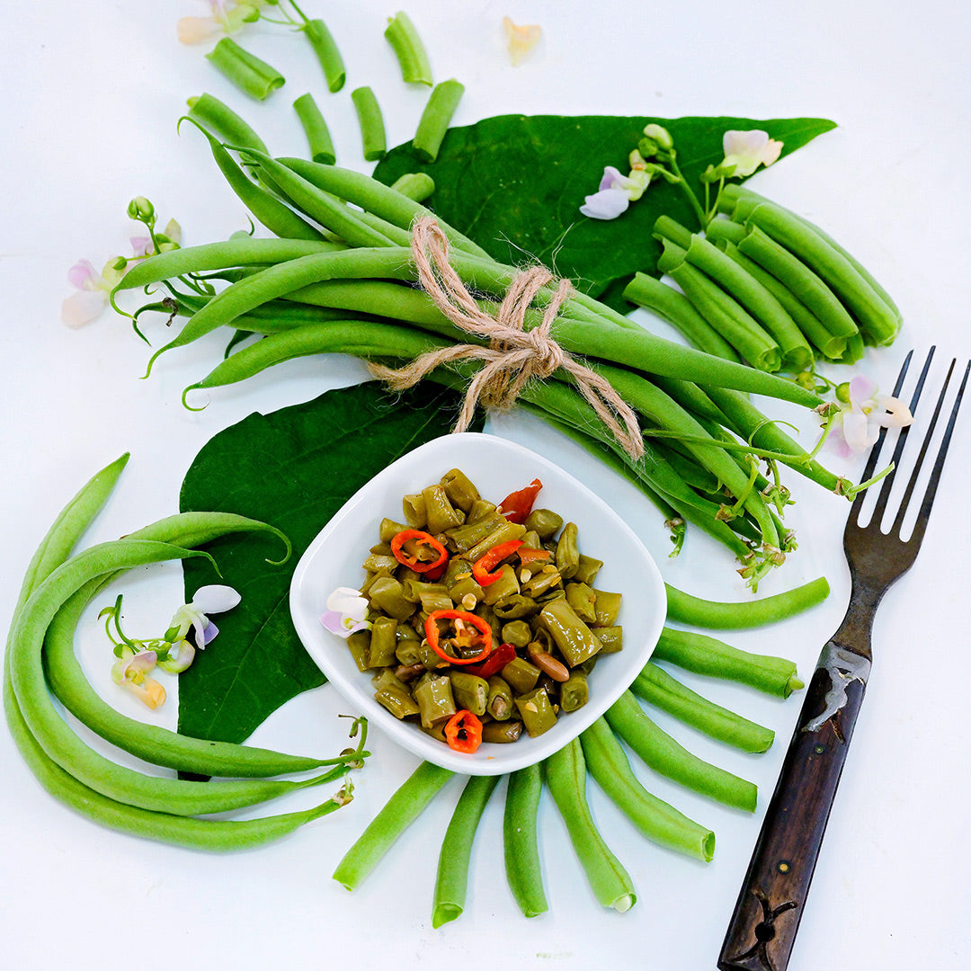 Whole and cut Calima Beans with pickled beans, blooms and foliage arranged on white background.
