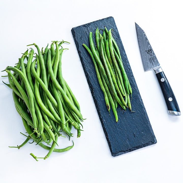 An overhead view of fresh and cooked Jade Bush Beans with a knife on a white background.