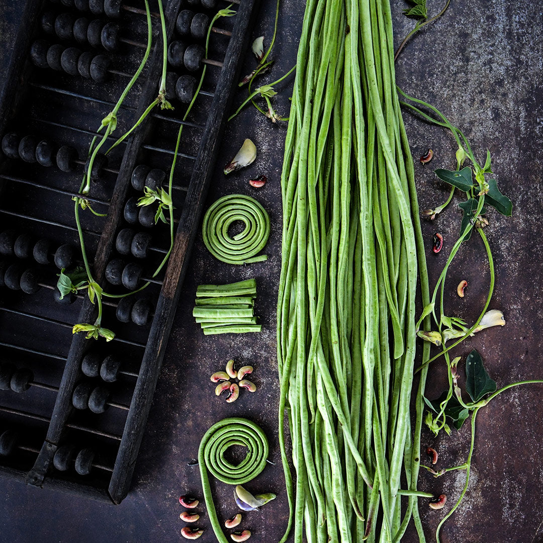 Bundled, chopped and whole Taiwan Yard-Long Beans with blooms on a dark brown background.