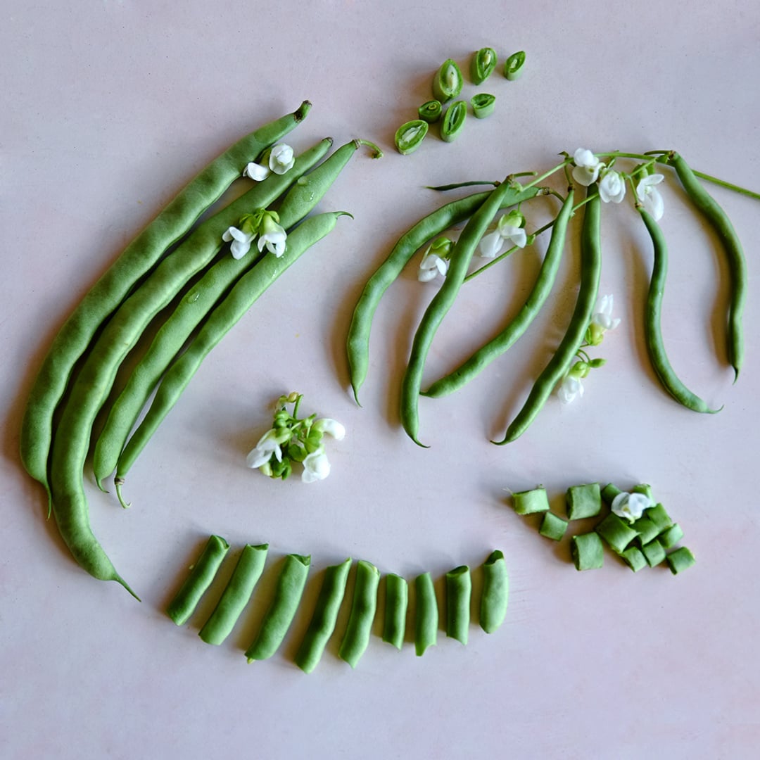 Cut and whole McCaslan 42 Pole Beans arranged with blooms on a light pink background.