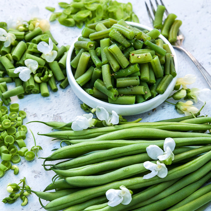 Cooked, raw, chopped and whole Odeon Bush Beans with white blooms on a light background.