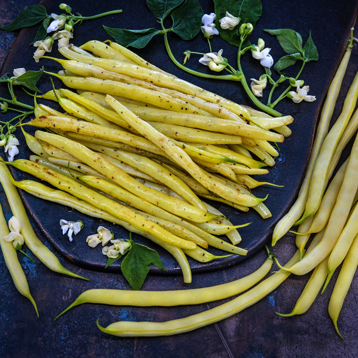 Cooked and raw Sonesta Wax Bush Beans with blooms and leaves on a dark background.