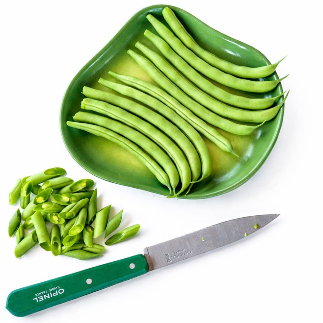 Cantare Beans on a green plate with chopped beans and green handled knife on a white background.