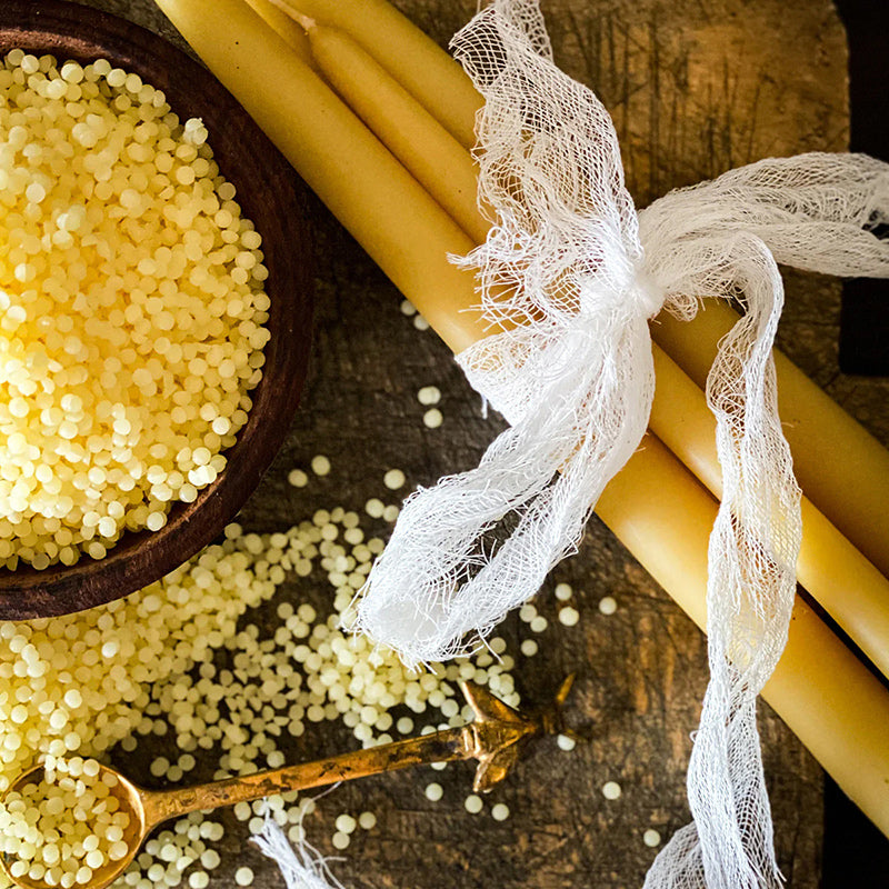 Beeswax Pastilles in brown bowl next to beeswax candles.