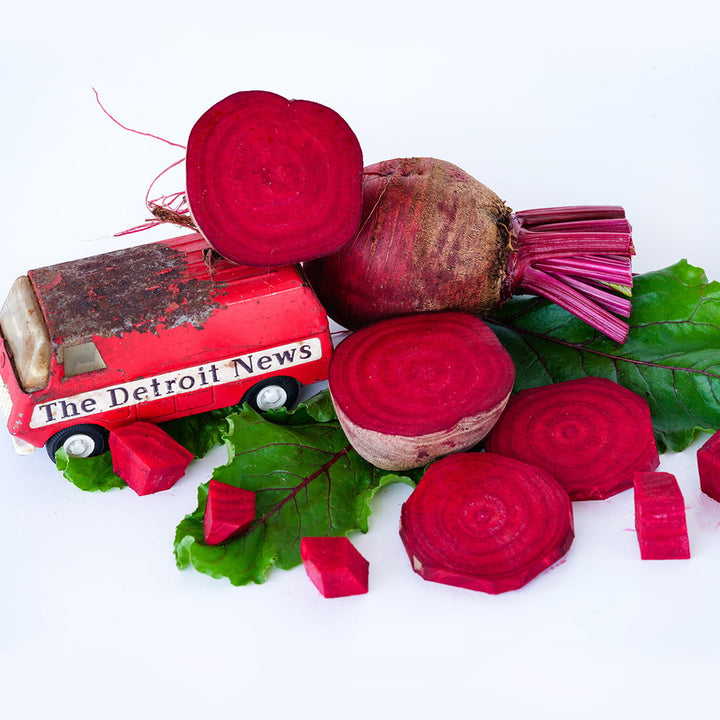 Cut and whole Detroit Dark Red Beets with a vintage Detroit News toy van on a white background.
