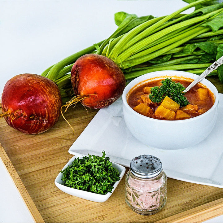 A bowl of Golden Beet borsch with a couple of whole beets on a wooden serving tray on white.