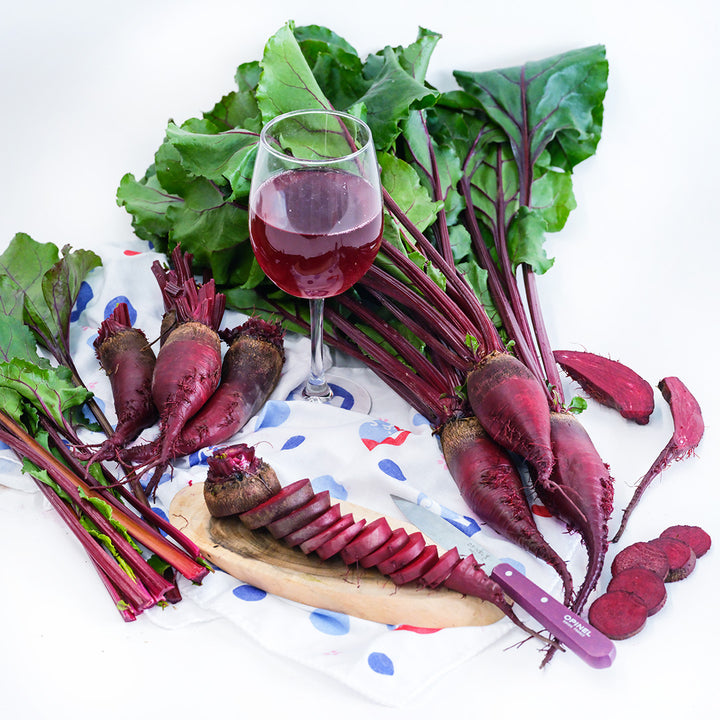 Sliced and whole Renova Beets arranged with a wine glass full of beet juice on a white background.
