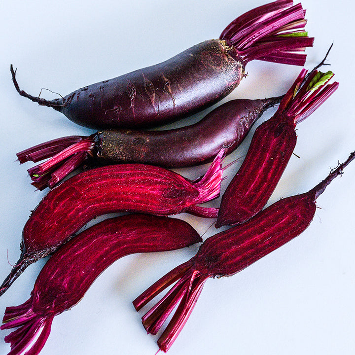 Whole and halved Cylindra (Formanova) Beets on a white background.