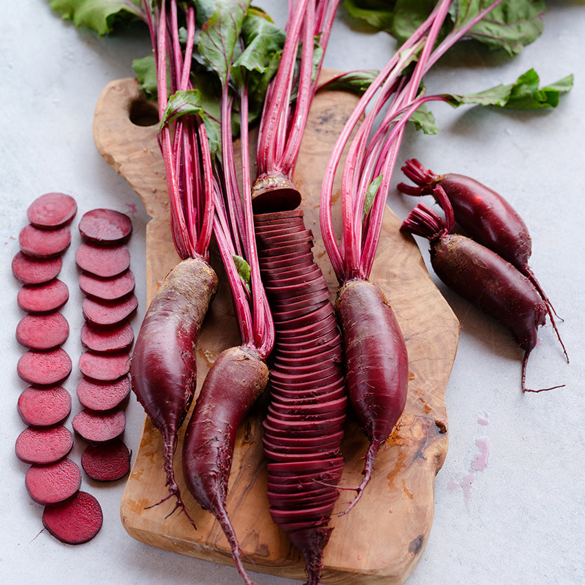 Sliced and whole Cylindra Beets on a wooden cutting board.