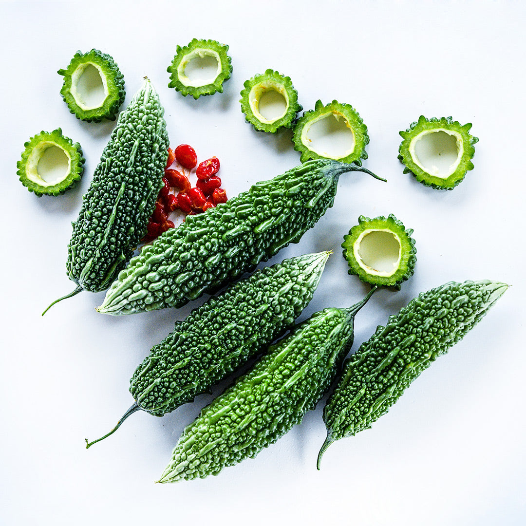 Whole and cut Abashi Bitter Melon arranged with seeds on a white background.