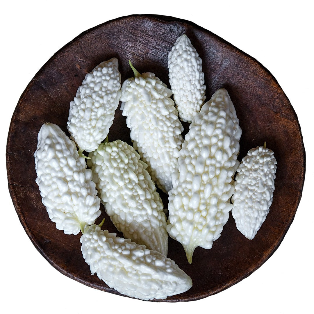 Several Jyunpaku Okinawan Pure White Bitter Melons in a wood bowl on a white background.