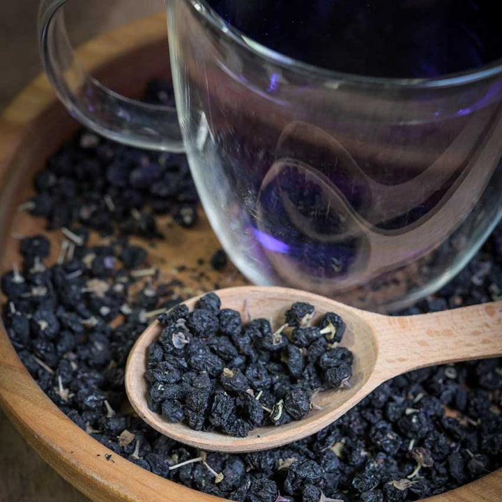 Black Goji Berry (Black Wolfberry) dried on a plate with a cup of Goji berry tea in the background.
