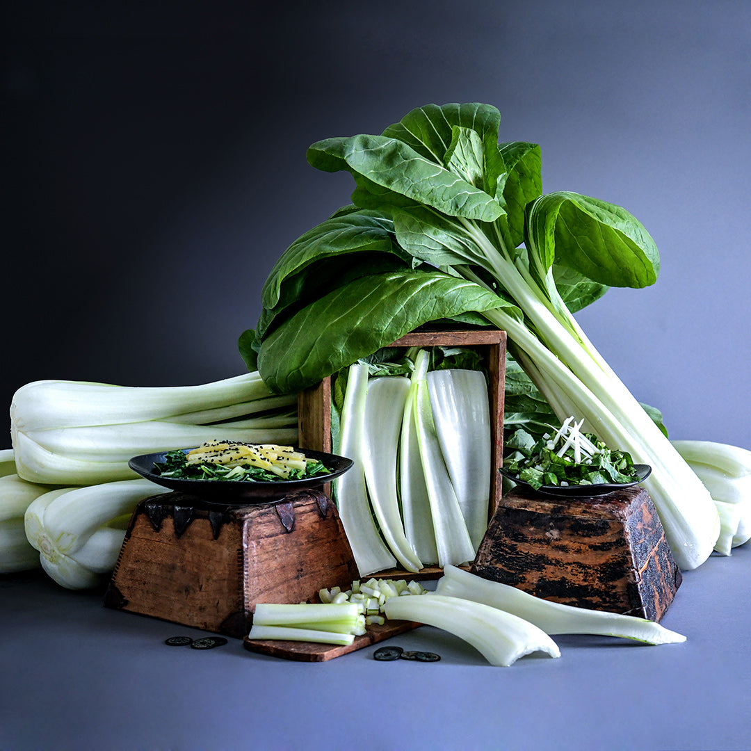Whole, cut and chopped Snow White Bok Choy with a couple of plated recipes on gray background.