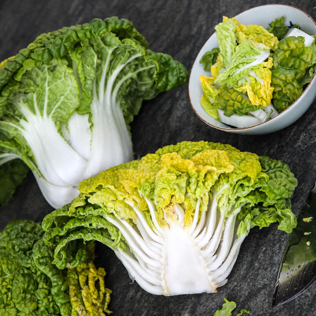 One whole and one half of Yellow Heart Winter Choy heads with leaves in a bowl on a stone background.