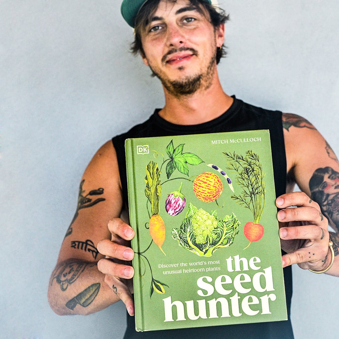 Author Mitch McCulloch holds out his book, The Seed Hunter, against a grey wall.