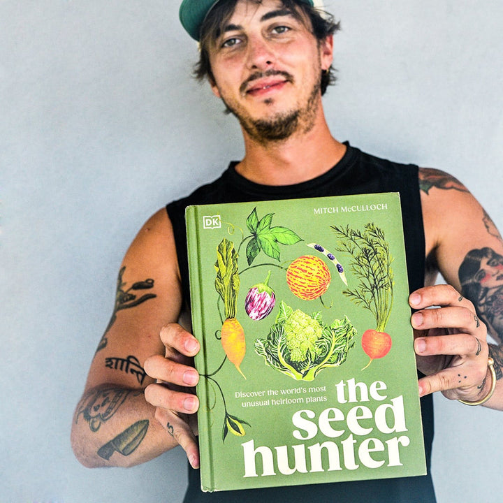 Author Mitch McCulloch holds out his book, The Seed Hunter, against a grey wall.