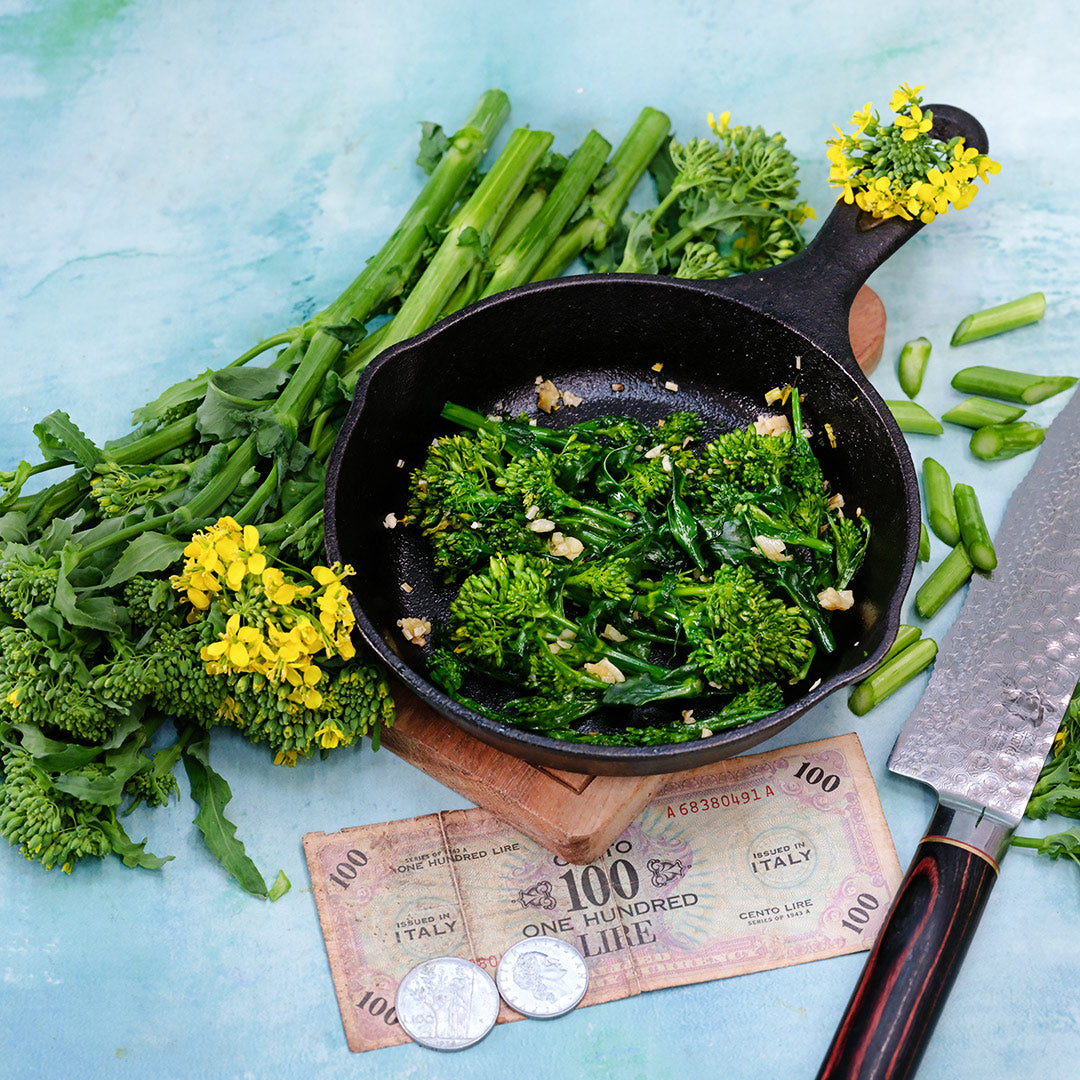 Cooked Natalina Di Fasano Cima Grande Broccoli Rabe in a cast iron skillet surrounded with fresh rabe.