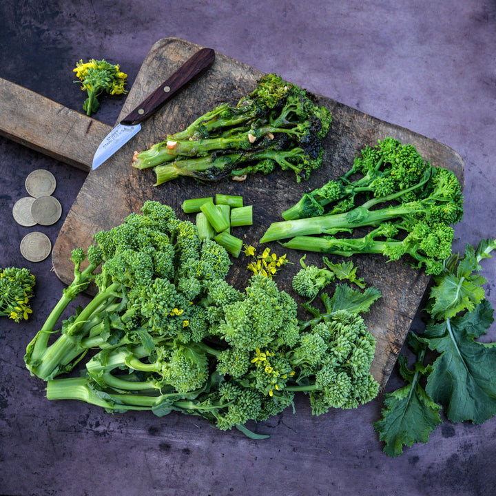 Cooked and fresh Natalina Di Fasano Cima Grande Broccoli Rabe on a wooden cutting board.