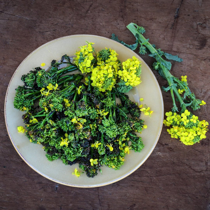 Cooked Rapini with blooms on a plate sitting on a vintage wooden background.