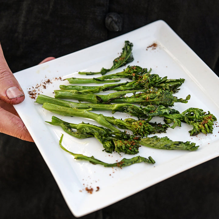 A man holding a grilled plate of gourmet Rapini.
