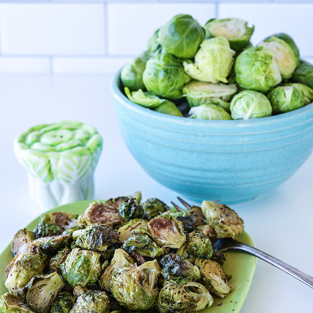 Roasted Long Island Improved Brussels Sprouts on a plate with a bowl of fresh Brussels Sprouts in the background.