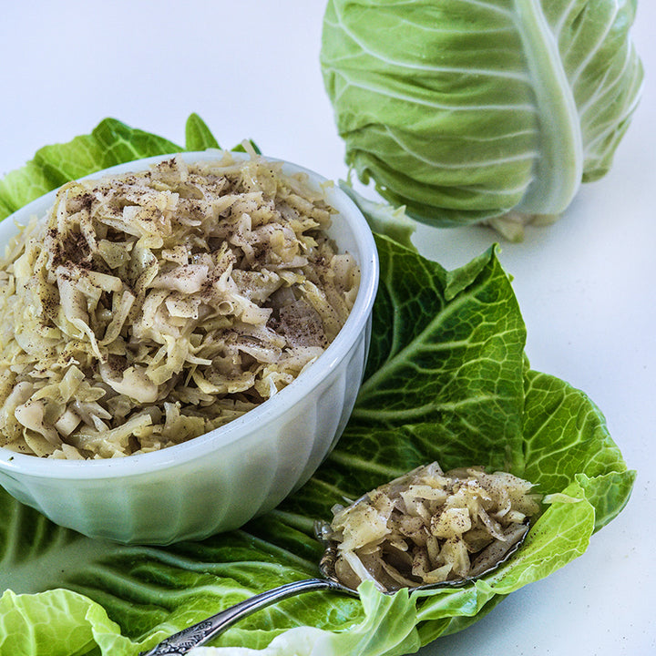A bowl full of Sauerkraut made from Filderkraut Cabbage rests on a cabbage leaf with spoon.