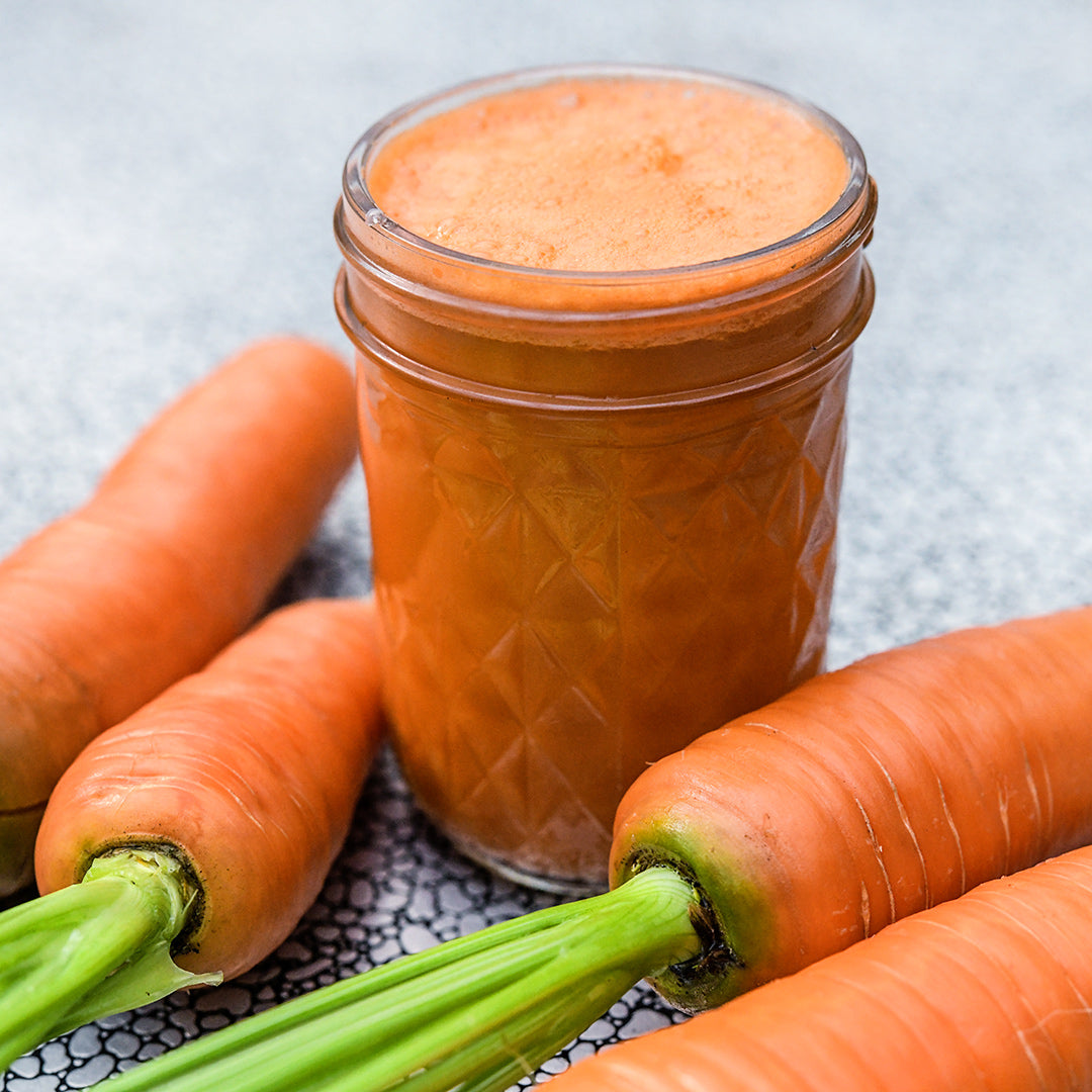 A mason jar full of Koral Carrot juice with whole carrots on a tray.