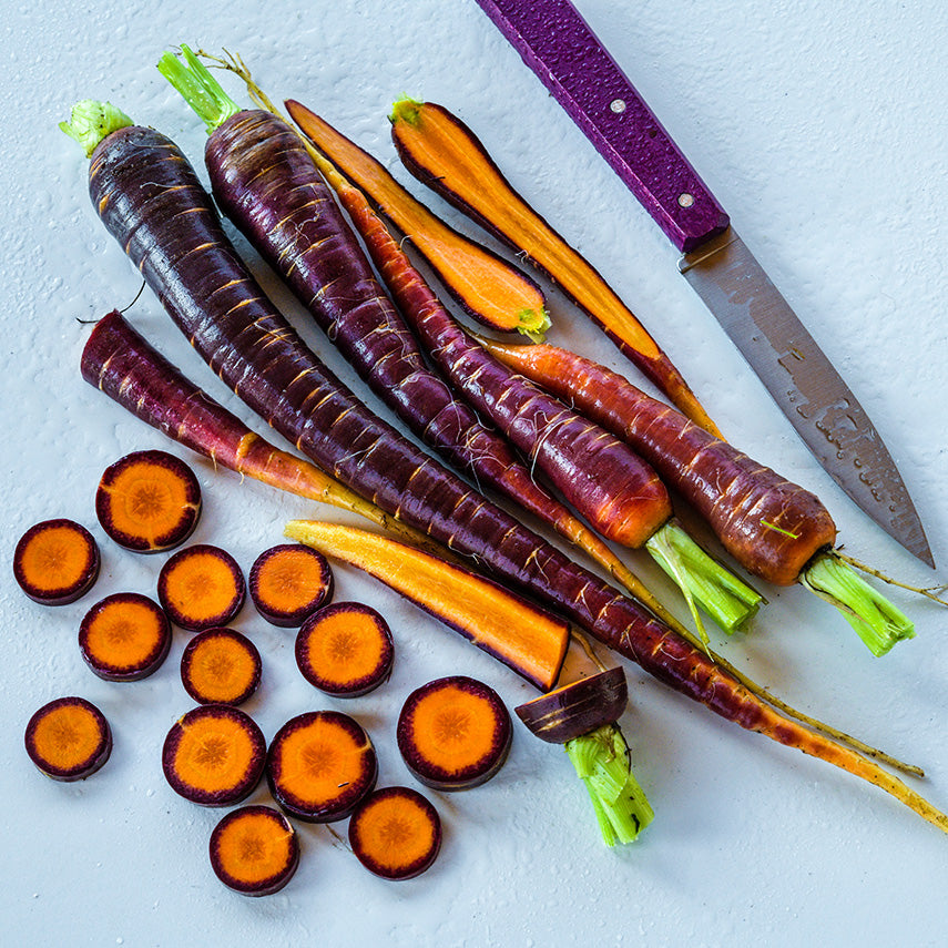 Sliced, cut and whole Lila Lu Sang Carrots with a purple handled knife on a white background.