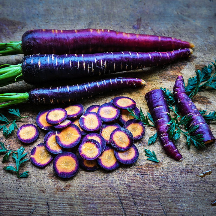 Whole and sliced Lila Lu Sang Carrots with foliage on wooden cutting board.