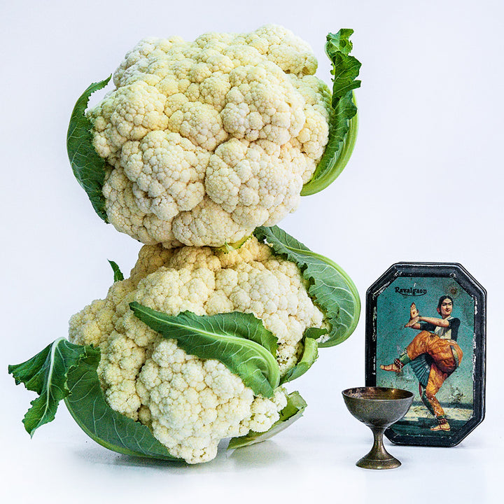 A couple of stacked heads of Durgesh 41 Cauliflower with items from India on a white background.