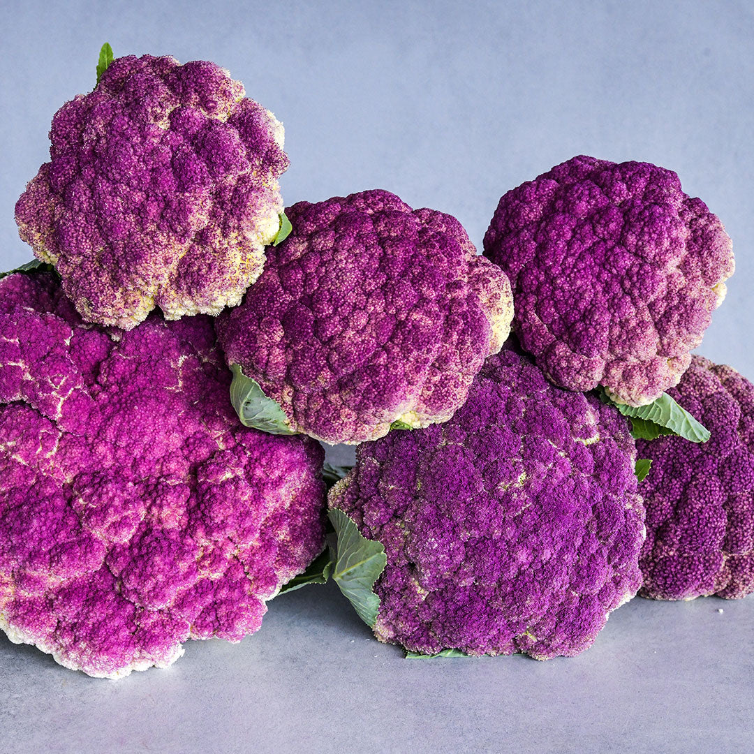 A half dozen Purple of Sicily Cauliflower heads stacked on a table.