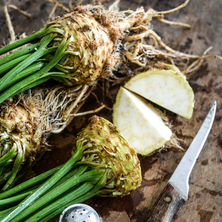A close-up of whole and cut Giant Prague Celeriac heads on a wooden cutting board.