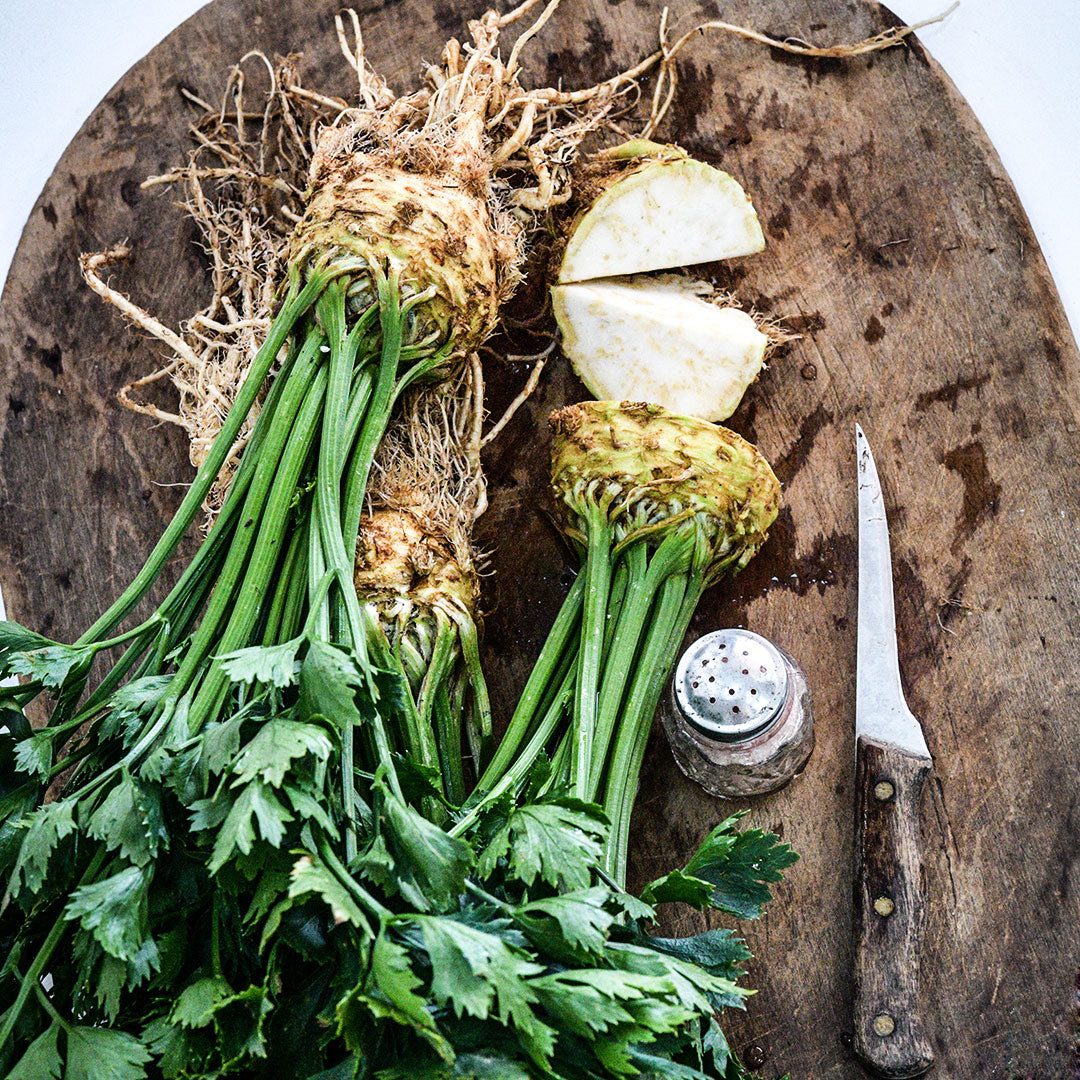 Overhead view of Giant Prague Celeriac heads on a wooden cutting board with a knife and salt shaker.