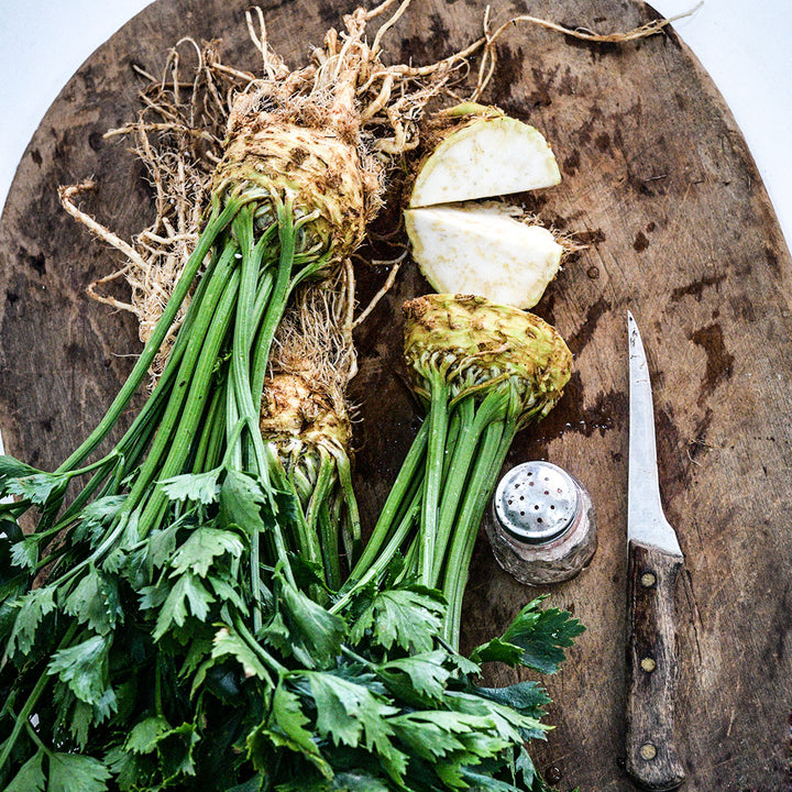 Overhead view of Giant Prague Celeriac heads on a wooden cutting board with a knife and salt shaker.