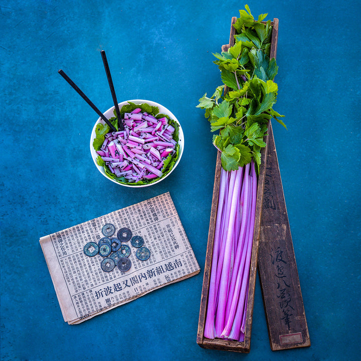 Chinese Pink Celery stalks in wooden box and cut celery in a bowl on a blue background.