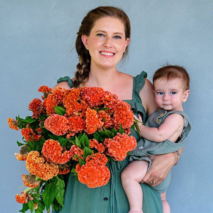 A smiling mother and son holding a giant bouquet Kumquat Orange Celosia.