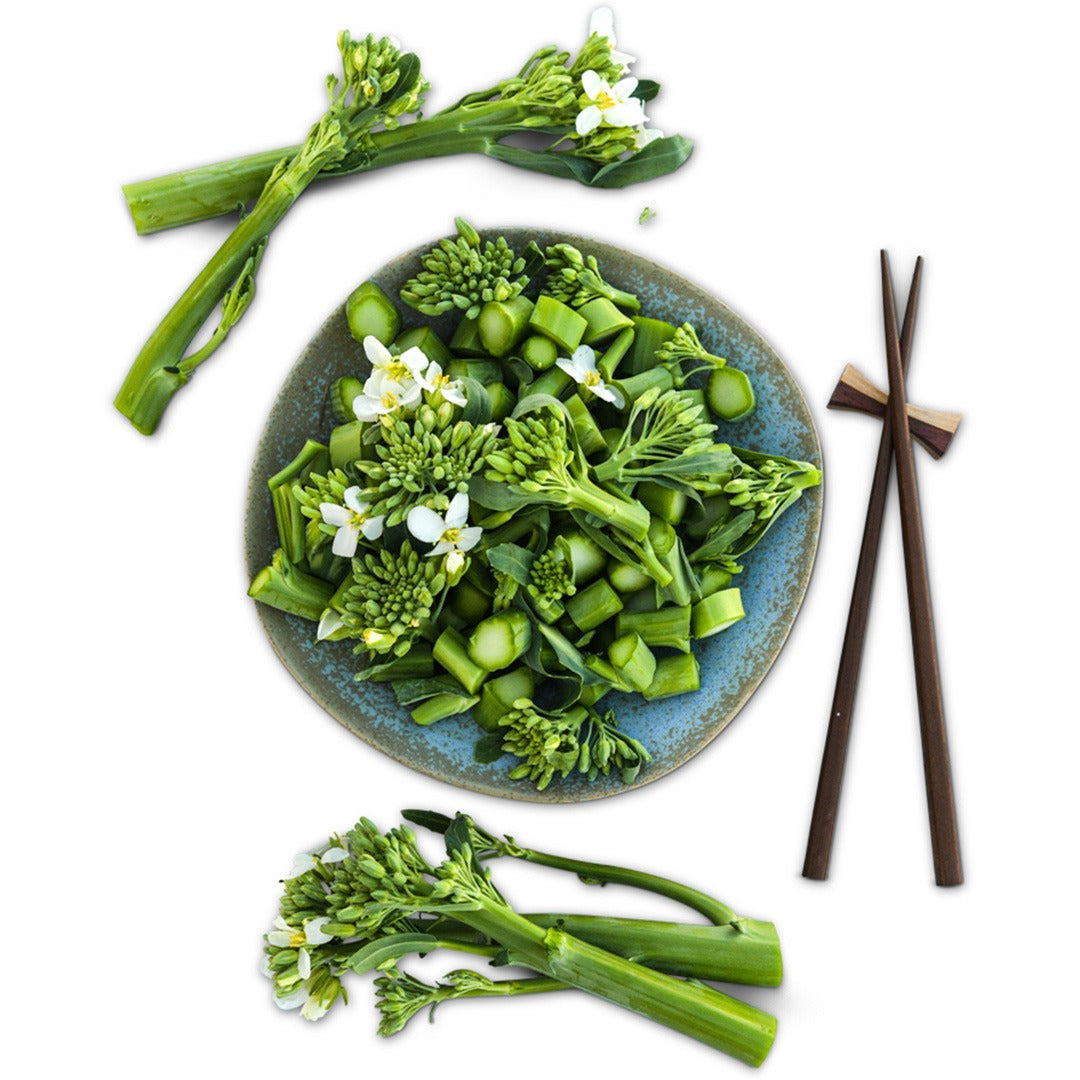 Chopped Yod Fah Chinese Broccoli greens and blooms in a ceramic bowl with chopsticks on a white background.