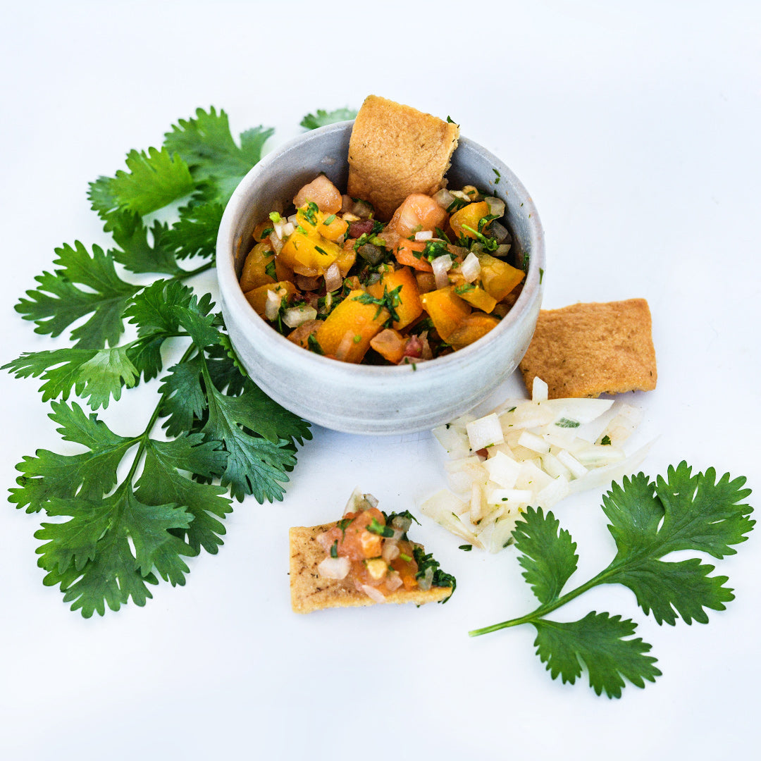 Slo-Bolt Cilantro leaves surrounding a small bowl of yellow tomato salsa with chips.