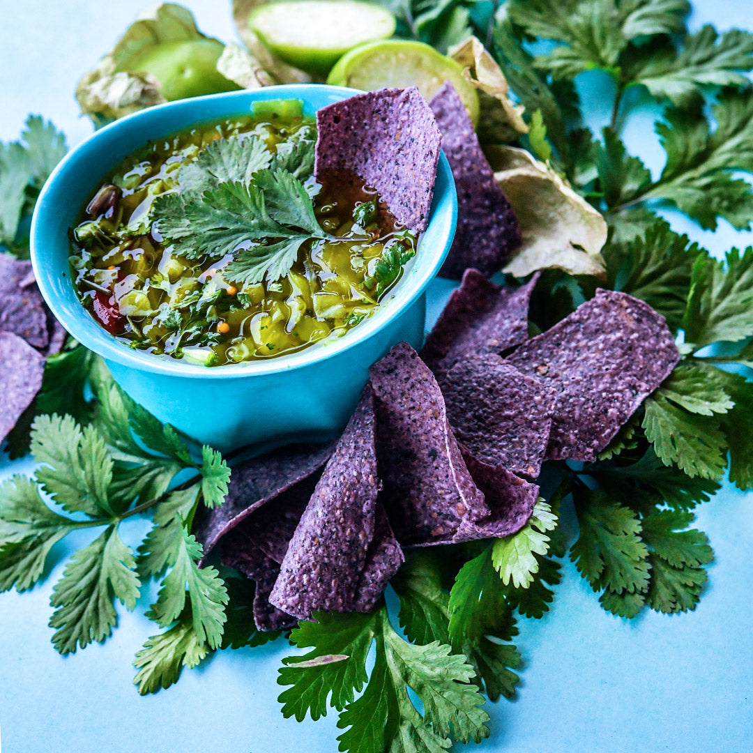 Slo-Bolt Cilantro leaves in green salsa in a blue bowl with purple chips.