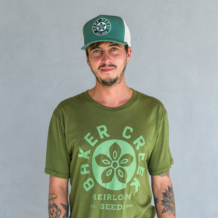 A smiling man wearing a Baker creek T-shirt and a Fern Green Baker Creek Organic Cap.
