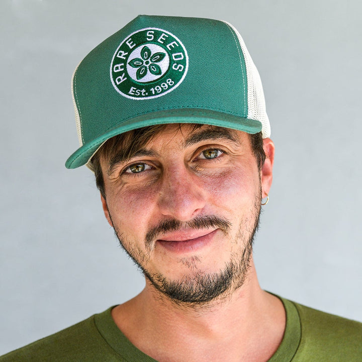 A man smiling while wearing a Fern Green Baker Creek Organic Cap against a grey wall.