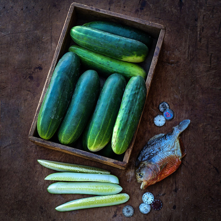 Ancash Market Cucumbers in a wooden box with slices and a piranha fish on a dark background.