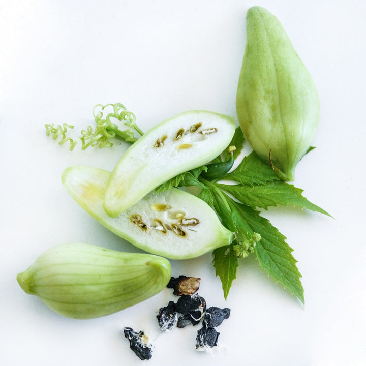 Cut and whole Lady Slipper Achocha fruits on leaves on a white background.